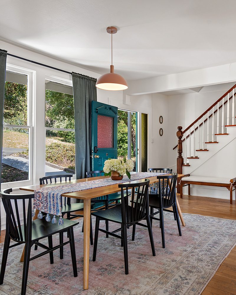 Dining room with black spindle chairs, pink pendant and a staircase beyond
