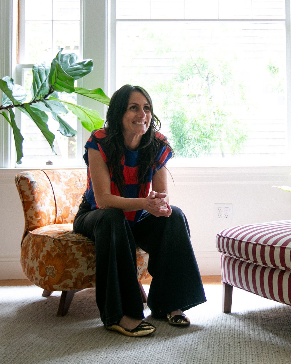 Laura, founder of Tannat Interiors, smiling on a floral chair in a sunlit room